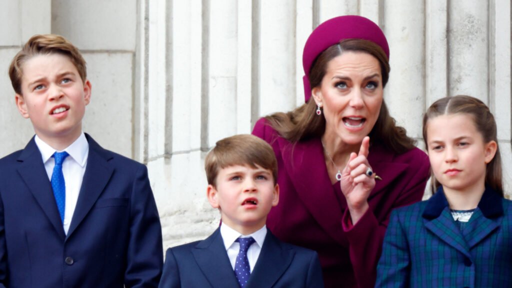 Kate Middleton looks stern while wearing a deep red coat dress and matching hat as she instructs children Prince George, Prince Louis, and Princess Charlotte