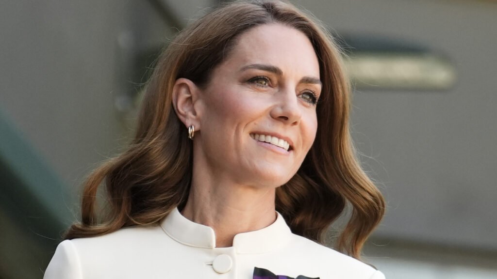 Kate Middleton has long brown wavy hair and wears a white dress