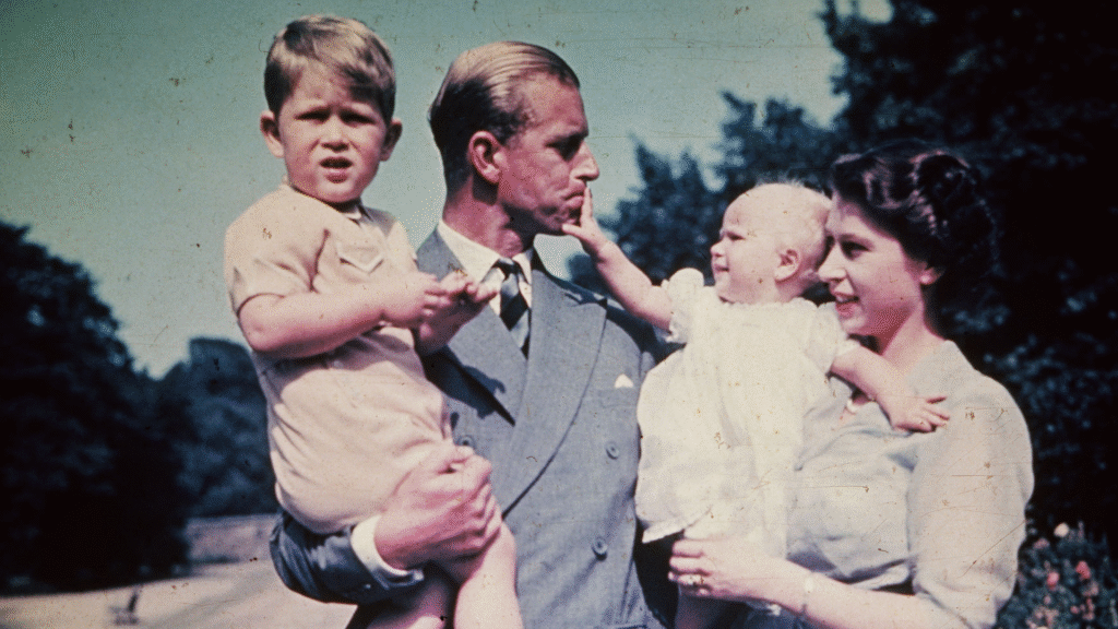Prince Philip holding Prince Charles while Princess Anne, held by Queen Elizabeth, pulls on his lip