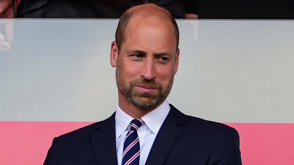 Prince William wearing a suit and tie in front of a pink and white background