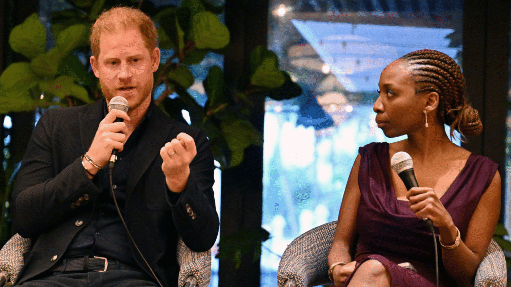 Prince Harry speaking into a mic sitting on stage next to Sophie Chandauka