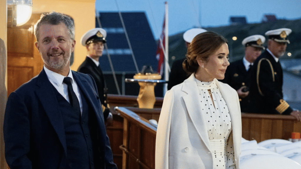 Queen Mary wearing a white polka dot dress and King Frederik in a suit standing on the royal yacht