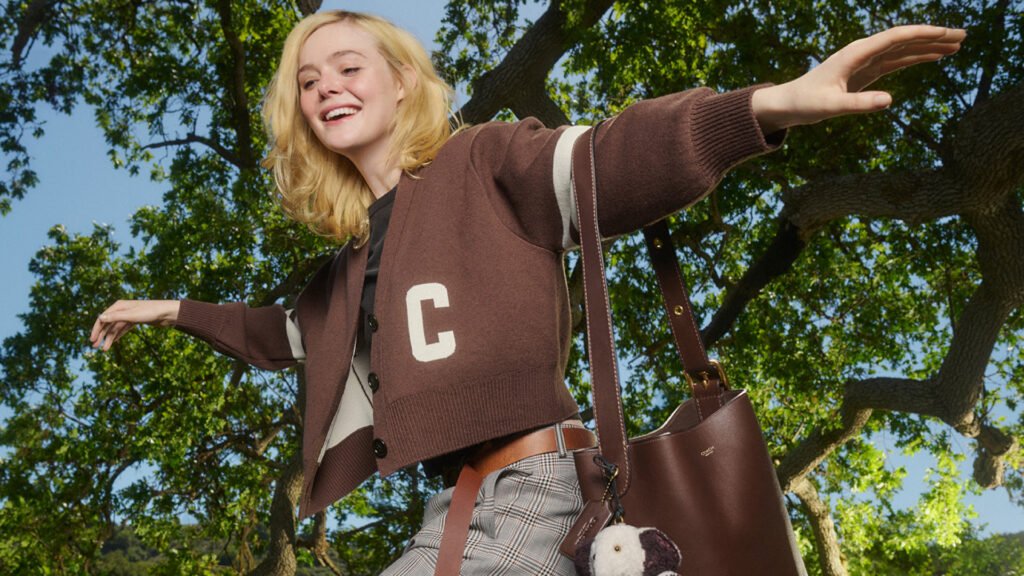 Elle Fanning in a tree wearing a Coach letter jacket and a bucket bag