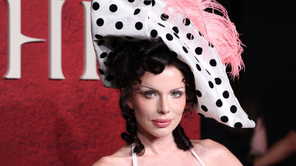 a white woman with dark hair wearing a white hat with black polka dots and a pink feature