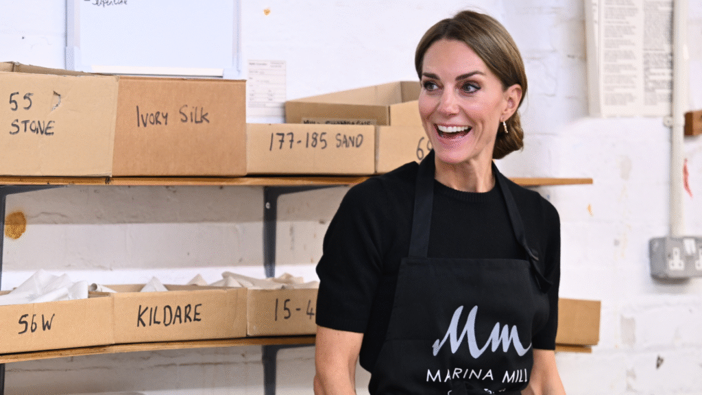 Kate Middleton wearing a black shirt and apron with her hair in a knot