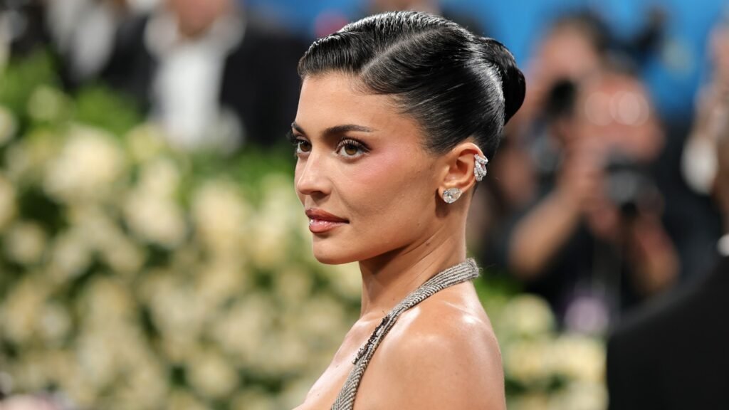 a woman photographed in front of a crowd wearing a tight bun and silver earrings